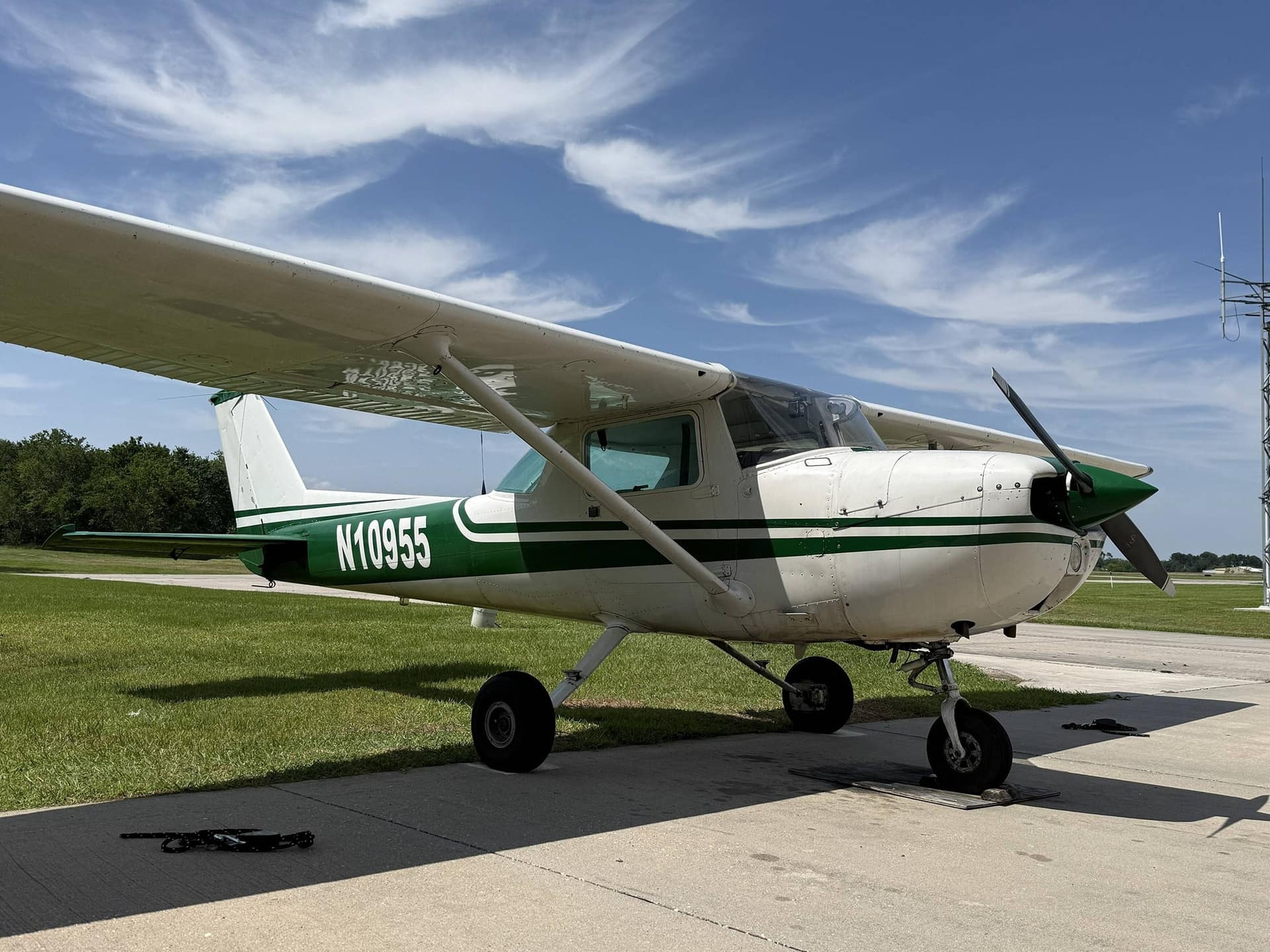 Cessna 150L N10955 in green and white, three-quarter view from the nose on a concrete pad beside grass.