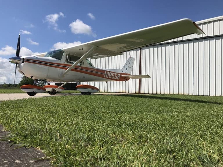 Cessna 150L N18558 photographed low from the grass beside a white hangar, stars painted on the fin.