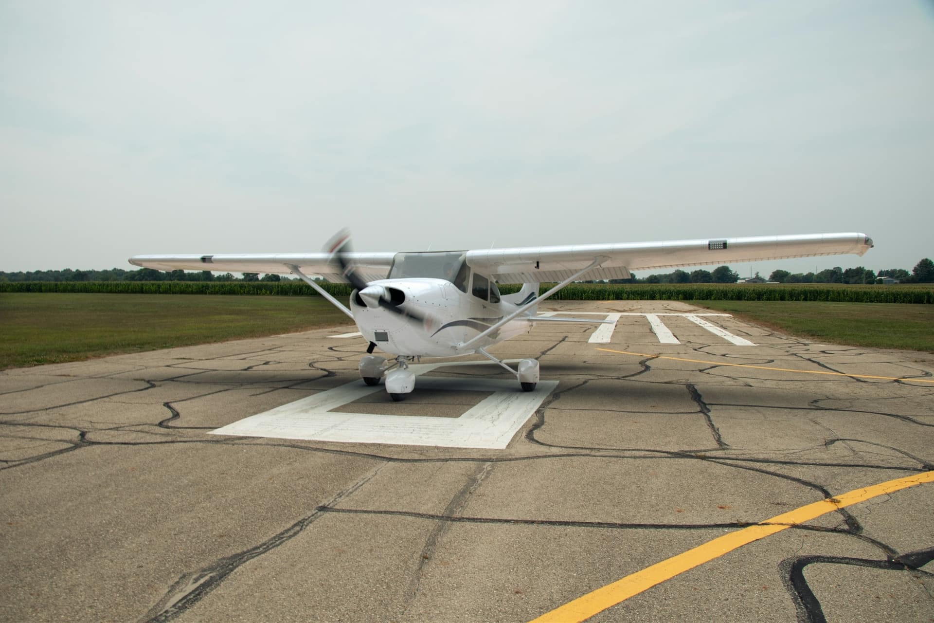 A four-seat high-wing Cessna facing the camera on a taxiway, propeller turning.